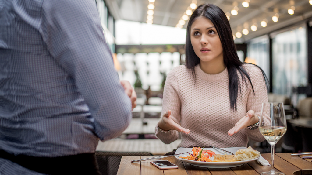 An unhappy restaurant guest gestures at her food to a service staff