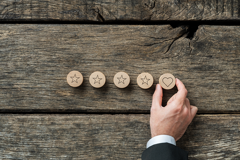 A male hand places four wooden stars and one wooden heart on a wood table.