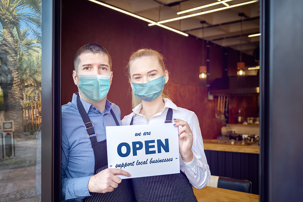 two restaurant employees wearing PPE masks holding an Open for Business sign