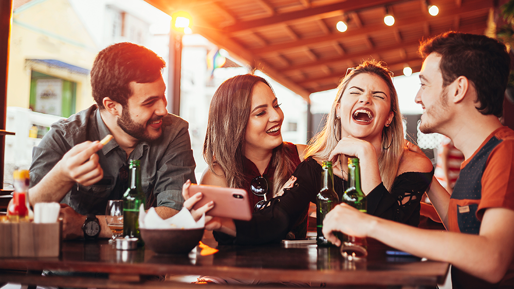 Four guests at a bar, having beer and snacks and laughing with one another.