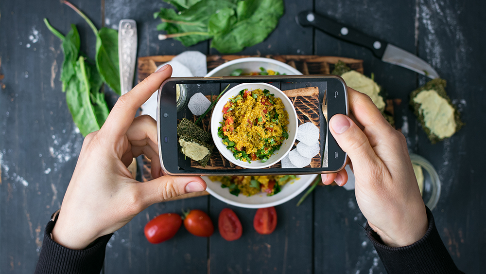 Overhead shot of hands holding a smart phone taking a photo of tasty restaurant food for Instagram