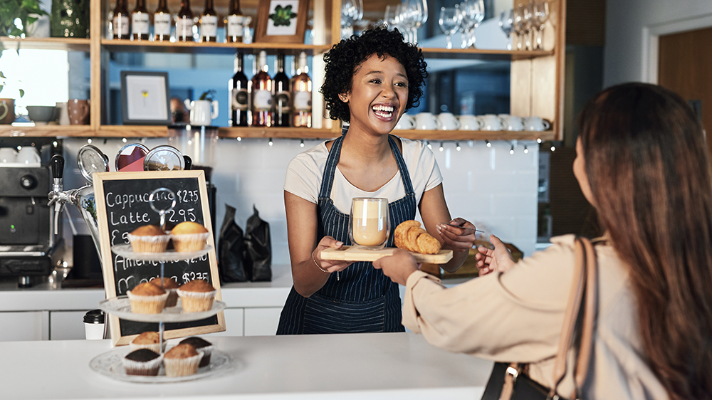 A smiling restaurant employee handing a food order over to a satisfied guest.