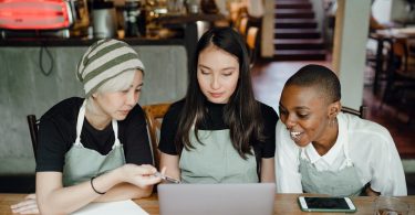 three cafe workers look on over a laptop