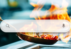 Internet search bar superimposed in front of a restaurant kitchen pan cooking with spurting flames