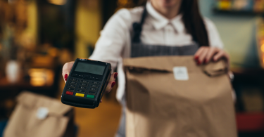 Waitress holding a restaurant to-go bag in one hand and a mobile POS system in the other