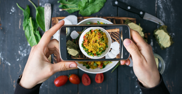 Overhead shot of hands holding a smart phone taking a photo of tasty restaurant food for Instagram