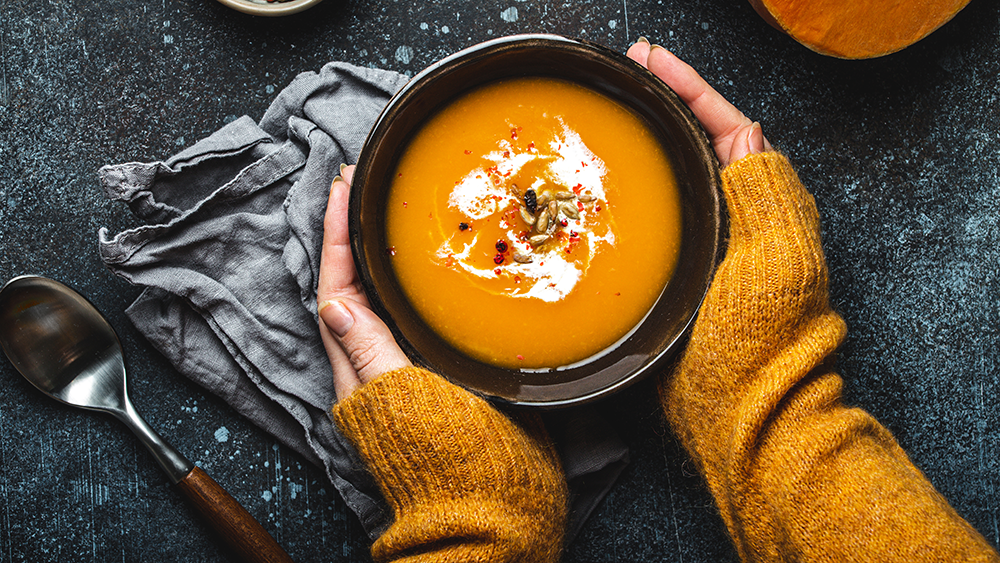 Overhead shot of an autumn-based dish soup being held by two hands in an orange sweater.
