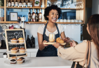 A smiling restaurant employee handing a food order over to a satisfied guest.