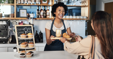 A smiling restaurant employee handing a food order over to a satisfied guest.