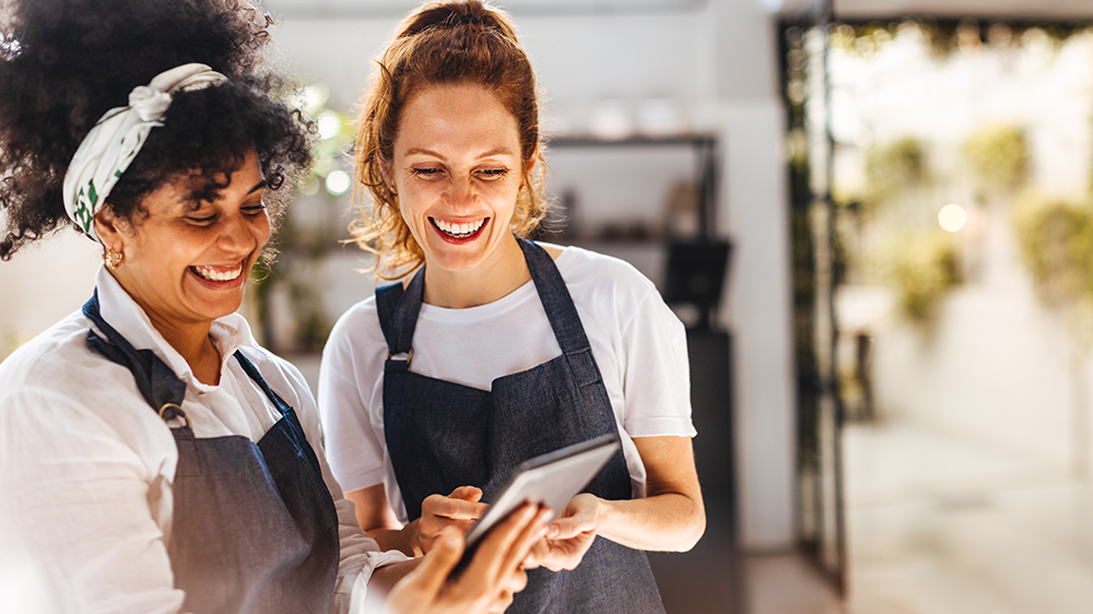 Two women restaurant workers collaborate while looking over a smart tablet.